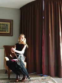 Young woman holding umbrella while sitting on chair at home