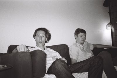 Portrait of friends sitting on sofa against wall