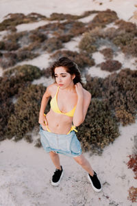 Carefree young woman in yellow bikini standing on sand at beach