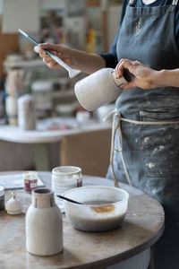Crop photo of woman artisan making earthenware vase preparing for paint with brush