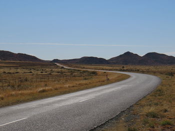 Road leading towards mountains against clear blue sky