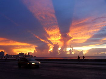 Silhouette city by sea against sky during sunset