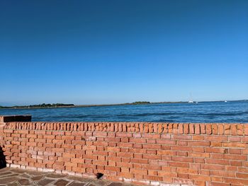 Stone wall by sea against clear blue sky