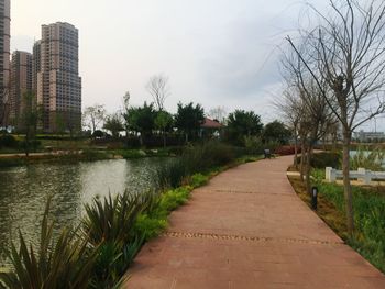 Footpath by river and buildings against sky