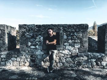 Full length of young man standing against stone wall