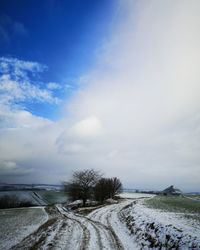 Road by snow covered landscape against sky