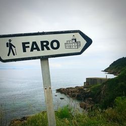 Road sign by sea against sky