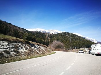 Road by trees against blue sky