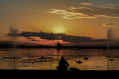 Silhouette people sitting by lake against sky during sunset