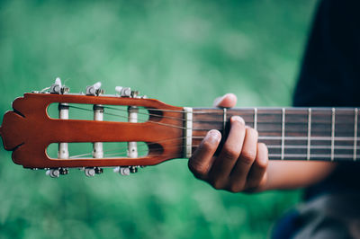 Cropped hand of person playing guitar over field