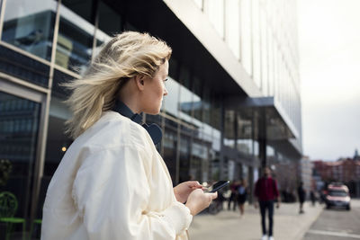 Side view of woman using mobile phone in city