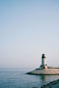 Lighthouse by sea against clear sky