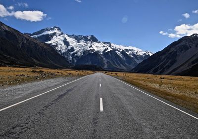 Empty road leading towards snowcapped mountains against blue sky
