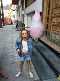 Full length of excited girl with candyfloss in city