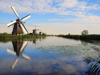 Traditional windmill by lake against sky