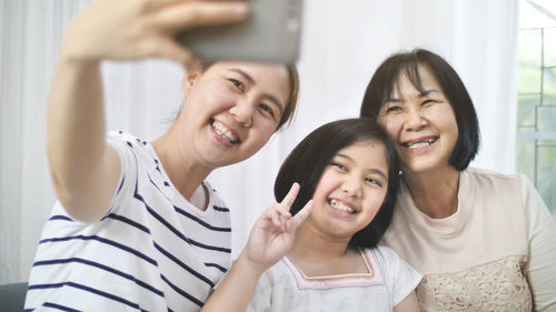 Smiling woman taking selfie with daughter and mother at home