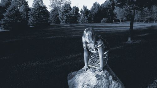 Cute girl kneeling on rock at park