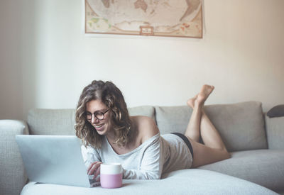 Young woman using phone while sitting on sofa at home