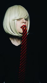 Mid adult woman with tie in mouth against black background