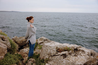 Young woman standing on rock by sea against sky