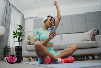 Side view of woman using mobile phone while sitting on sofa at home