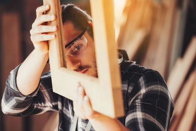 A young male carpenter builder working overall equals a wooden bar with a milling machine in work