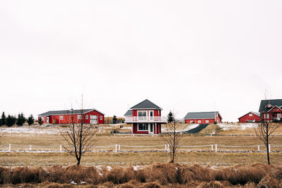 Houses and trees on field against clear sky