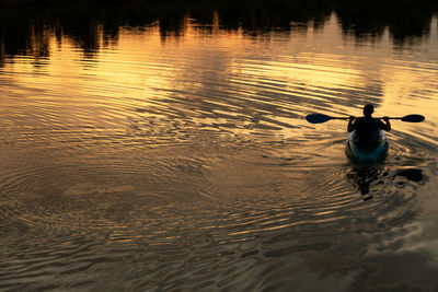 Rear view silhouette of man kayaking on lake during sunset