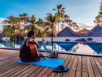 Man sitting by swimming pool against sky