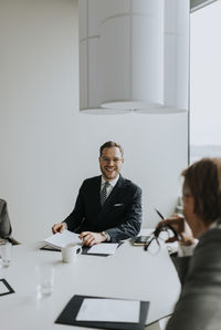 Smiling young businessman looking at colleague while sitting in board room