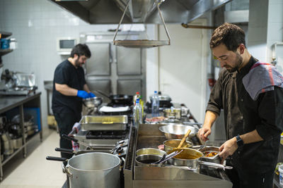 Chef standing by kitchen counter with coworker cooking in background at kitchen