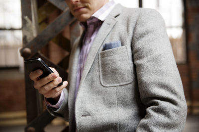 Midsection of businessman using smart phone while standing in empty warehouse