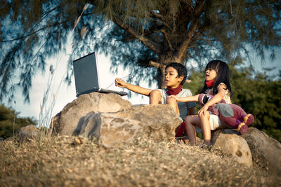 Friends sitting by plants against trees
