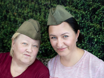 Portrait of smiling mother and daughter wearing hats against plants