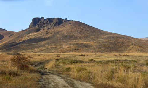 Dirt road leading towards mountains against clear sky