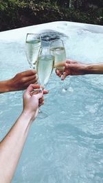 Cropped hands of friends toasting champagne flutes over swimming pool