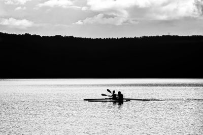 Silhouette people on boat in river against sky