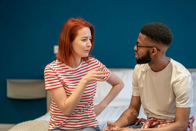 Young interracial couple husband and wife sit on bed at home discussing intimacy issues