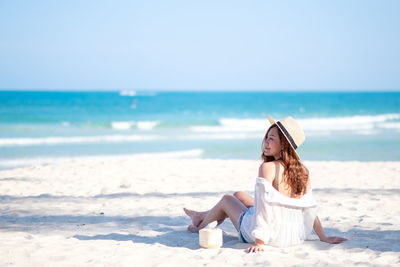 Rear view of woman wearing hat sitting at beach