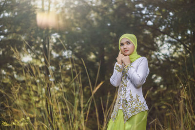 Beautiful young woman standing against plants and trees