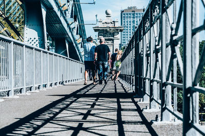 Rear view of people walking on footbridge in city