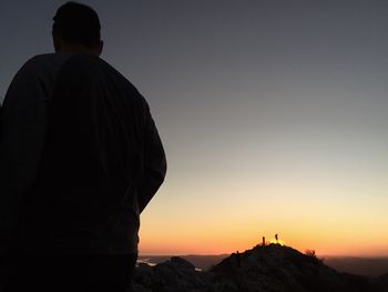 Rear view of silhouette man standing on mountain against sky during sunset