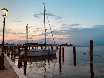 Sailboats moored in harbor at sunset