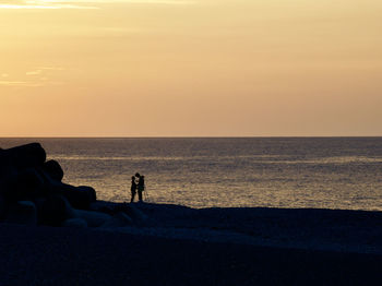 Silhouette people on beach by sea against sky during sunset