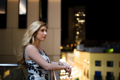 Close-up of young woman standing against illuminated building at night