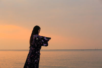 Woman in kimono standing by sea against sky during sunset