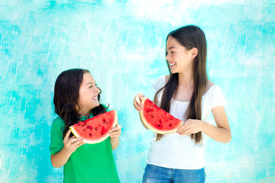 Happy female friends holding watermelon slices against turquoise wall