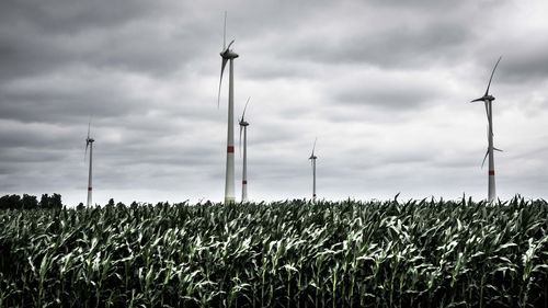 Wind turbines on landscape against cloudy sky