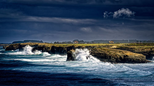 Scenic view against sky of sea with big waves crashing against rocks 