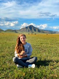 Beautiful young woman sitting on field against sky